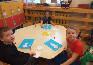 Zdjęcie przedstawia dzieci, wykonujące pracę plastyczną z bałwankiem.