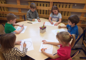 Zdjęcie przedstawia dzieci, dorysowujące dowolne elementy do konturu koła, tak aby stworzyć obraz własnego pomysłu.