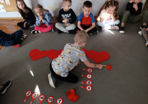 Chłopiec z grupy „Misie” rozwiązuje zadanie matematyczne przy pomocy serduszek walentynkowych.