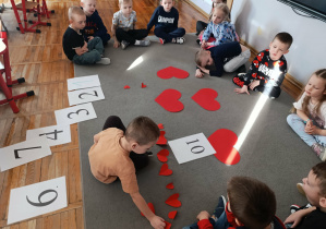 Chłopiec z grupy „Misie” rozwiązuje zadanie matematyczne na walentynkowych serduszkach.