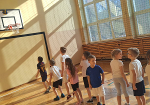 Dzieci stoją w kolejce i rzucają piłkę do kosza.