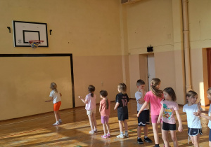 Dzieci ustawieni jeden za drugim i rzucają piłkę do kosza.