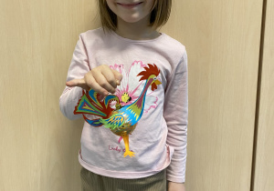 Wyróżniona dziewczynka pozuje z wykonaną przez siebie ozdobą – kolorowym kogucikiem.