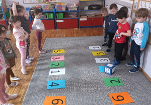 Dzieci rzucają kostką i stają na kartce z odpowiednią cyfrą