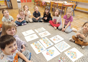 Dzieci siedzą w kole i oglądają obrazki z folkowymi wzorami.