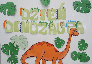 Tablica z napisem Dzień Dinozaura oraz ozdobami - dinozaurem i liśćmi.