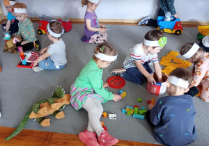 Przedszkolaki w czasie zabaw swobodnych na dywanie z wykorzystaniem dinozaurów.