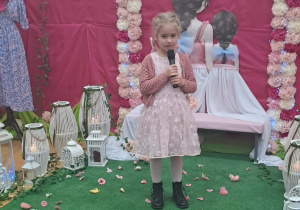 Dziewczynka trzyma mikrofon w tle dekoracji.