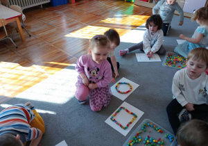 Dzieci układają kontur figur z kolorowych koralików.