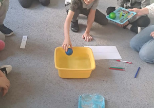 Chłopiec wrzuca piłkę do miski z wodą.