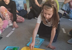 Dziewczynka wrzuca piórko do miski z wodą.