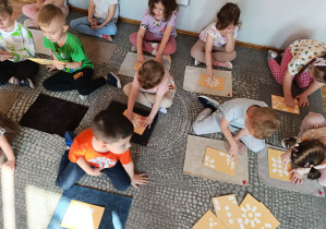 Dzieci siedzą przed dywanikami i układają geometryczne wzory