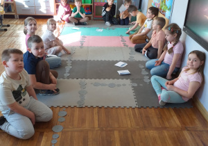 Dzieci układają kamienie w postaci ponumerowanych szarych kół różnej wielkości po kolei od kamienia numer 1 do kamienia numer 10.