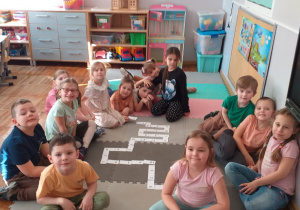 Dzieci pozują do zdjęcia na tle ułożonego przez siebie domina z kropkami i liczbami.