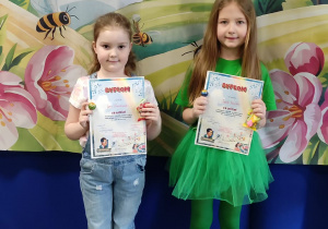 Dziewczynki występujące w konkursie wokalnym pozują z otrzymanymi dyplomami na tle dekoracji z napisem „Witaj Wiosno”.