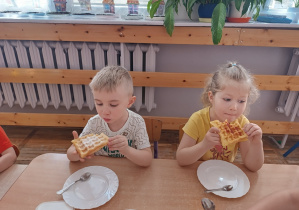 Dziewczynka i chłopiec jedzą gofry z dżemem i cukrem pudrem.