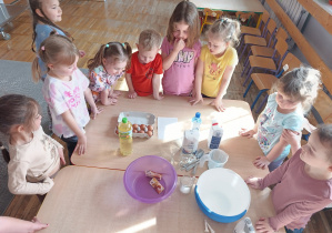 Dzieci stoją wokół stołu i oglądają składniki potrzebne do robienia gofrów.