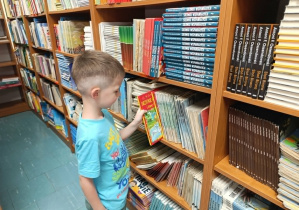 Chłopiec z grupy „Misie” podczas wypożyczania książki z biblioteki szkolnej.