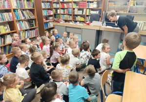 Przedszkolaki słuchają pani bibliotekarki opowiadającej o pracy w bibliotece.