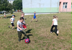 Na zdjęciu widzimy grupę dzieci grającą w piłkę nożną