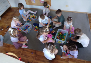 Dzieci siedzące na dywanie bawią się klockami.