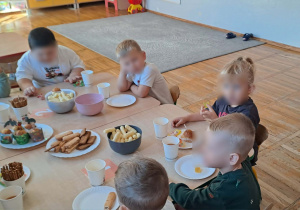 Dzieci siedzą przy stole na którym przygotowany jest poczęstunek.