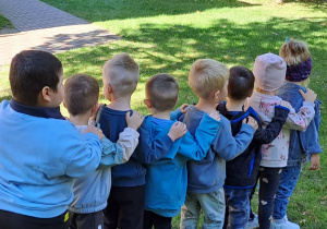 Dzieci stoją jedno za drugim, trzymając się za ramiona.