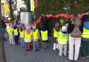 Dzieci z grupy Żabki wieszają łańcuch serc przy pomniku Jana Pawła II.