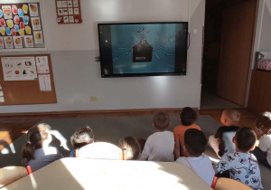 Dzieci siedzące przed tablicą multimedialną podczas oglądania historyjki o poczcie.