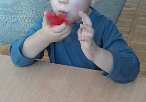 Chłopiec delikatnie dmucha na piórko.