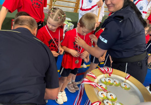 Pani Policjant zakłada medale na szyję naszym przedszkolakom, gratuluje przy tym sukcesu.