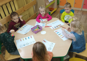 Krasnoludki przy stoliczku wykonują karty pracy. Muszą dopasować właściwy kolor kredki do przedmiotu w tym samym kolorze.