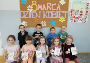 Liski świętują Dzień Kobiet - Dziewczynki z upominkami i dyplomami siedzą na krzesłach, a za nimi stoją chłopcy.