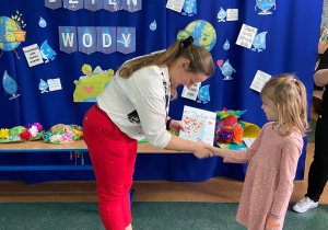 Zdjęcie przedstawia dziewczynkę, która otrzymuje nagrodę