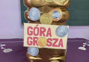 Zdjęcie przedstawia skarbonkę z napisem „Góra Grosza”.