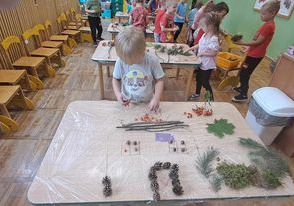 Dzieci układają na stolikach pejzaż z darów jesieni.