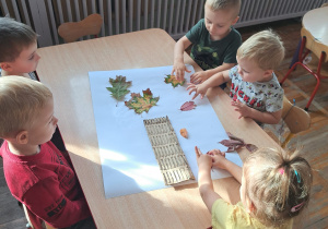 Dzieci z grupy Biedronki wspólnie wykonują pracę plastyczną przy stoliczku.